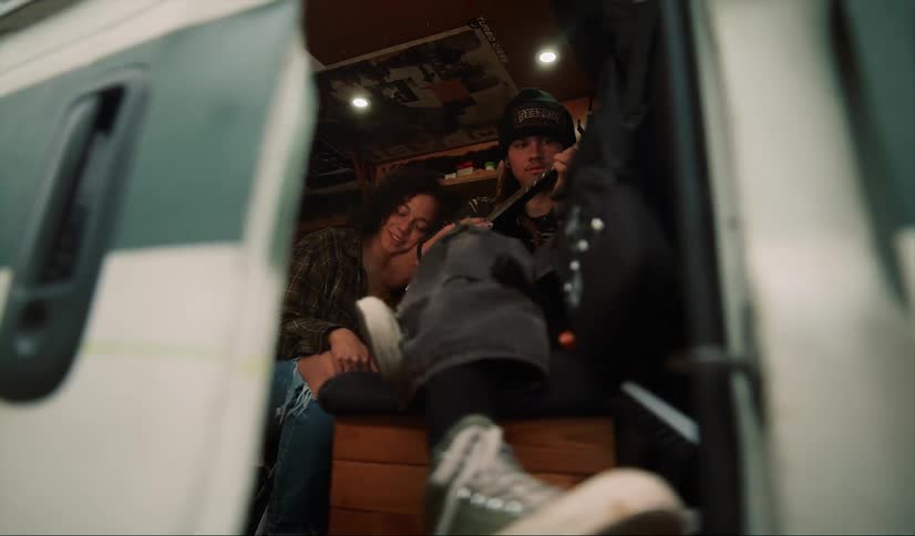 Young couple sitting on the back of a van playing guitar