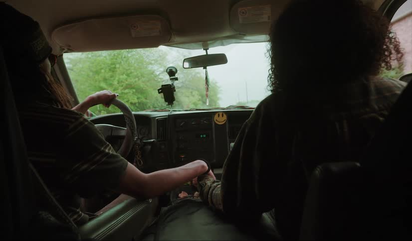 A woman sitting in the passenger seat holds her hand out and her boyfriend takes it while driving