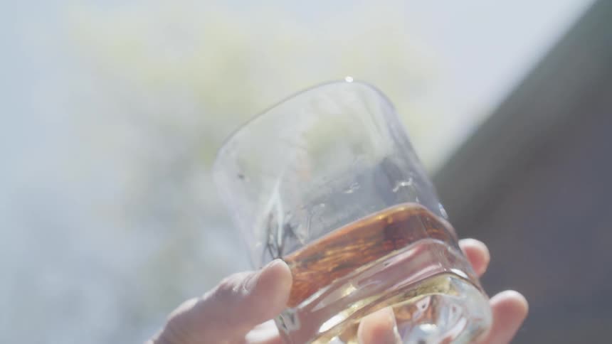 A hand holding a glass with amber liquid and a smoking flaming sprig