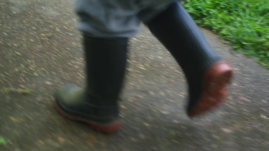 Boy with gray pants and green boots walks down road