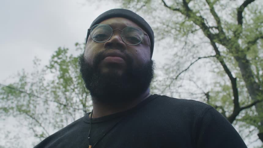 A man standing outside looking down with tree branches behind him