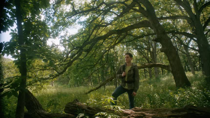 A man takes off his backpack and sits against a log taking a break from his hike