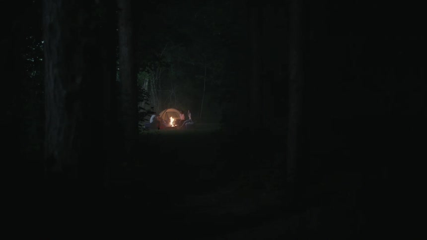 People sitting at a camp site around a camp fire and tent