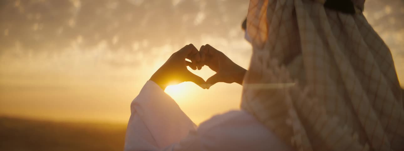 A woman holds her hands in the air and puts her fingers together to make a heart shape around the sun