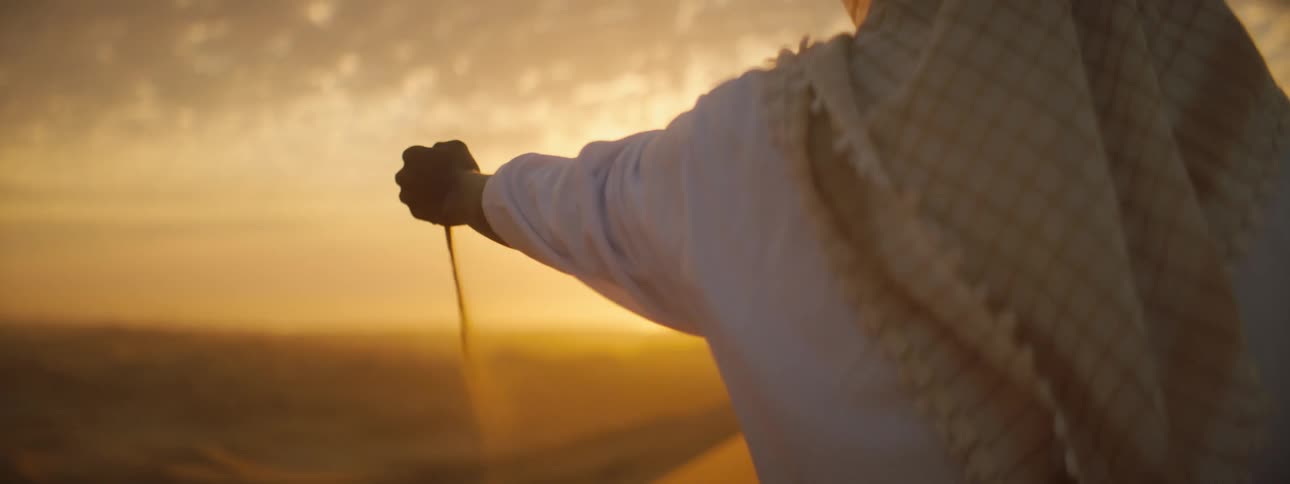 A woman bends down and picks up sand and lets it run through her fingers