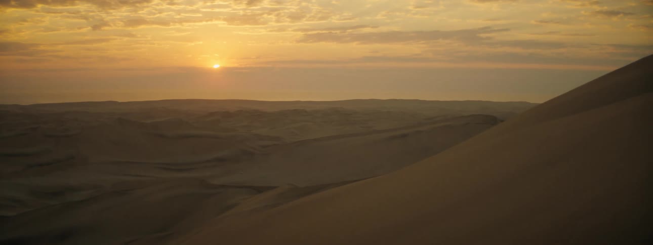 The sun setting over sand dunes in a remote desert