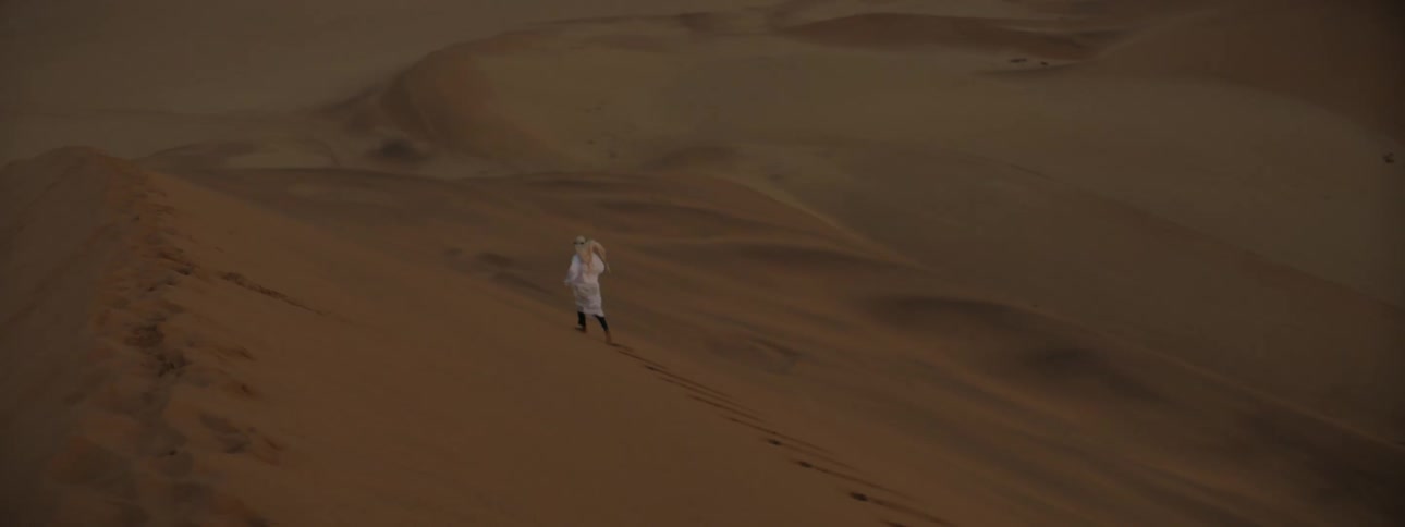 Aerial view of a person in a robe and turban running across a desert