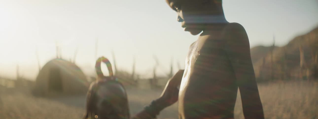 A woman touches her son on his bare chest and back as they sit outside their hut