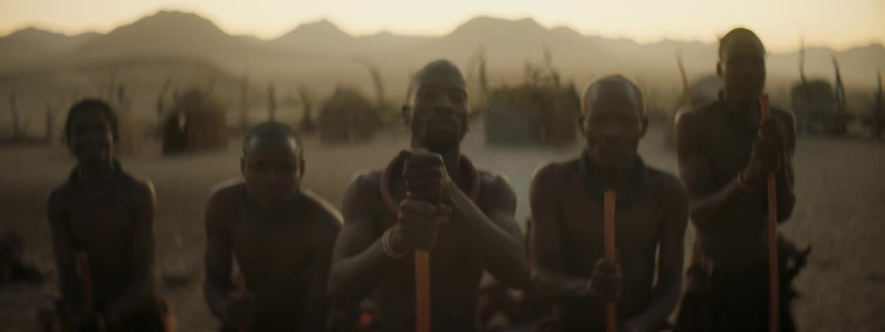 Men tap ground with staffs in village near mountains