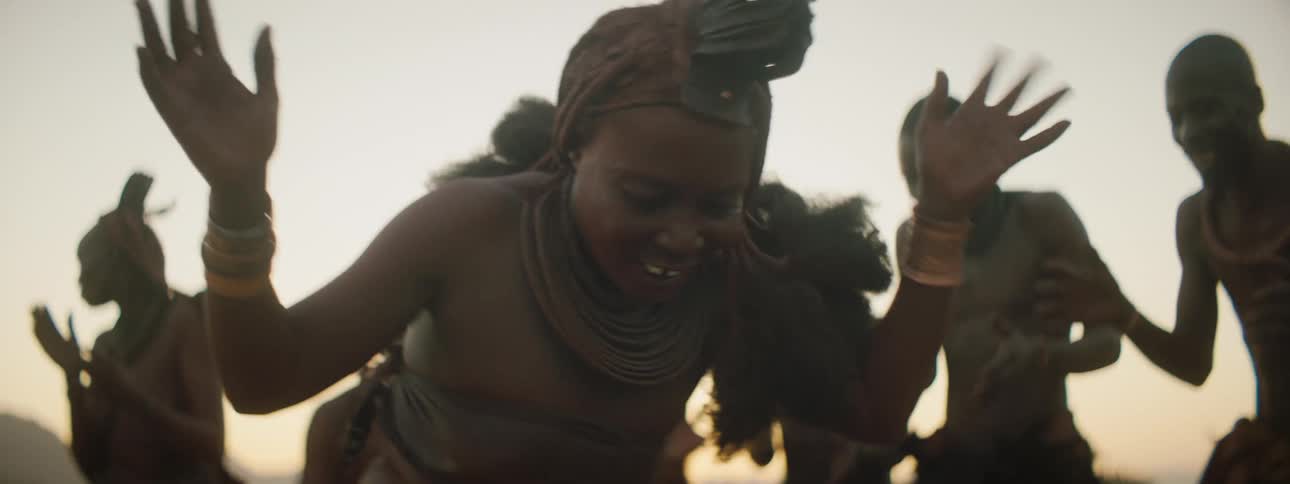 A black tribal woman dances while the surrounding crowd claps and cheers her on