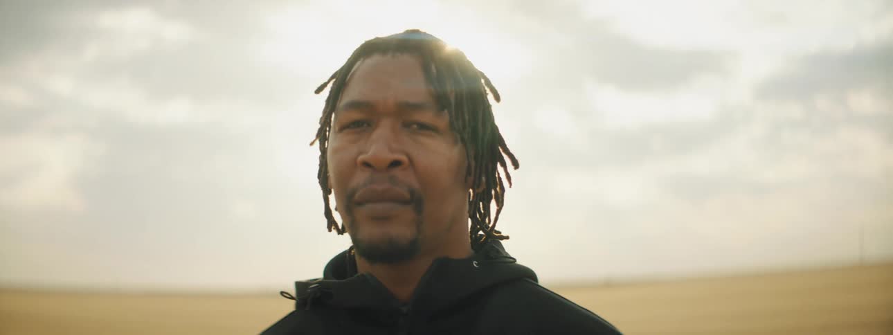 Man with a goatee and braids looks at the camera