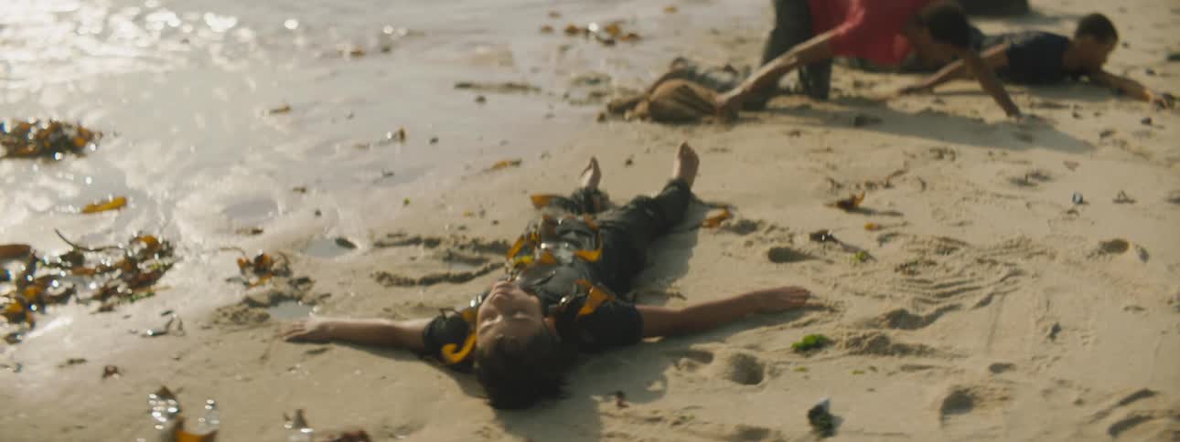 A persons is passed out on the beach as others crawl from the water