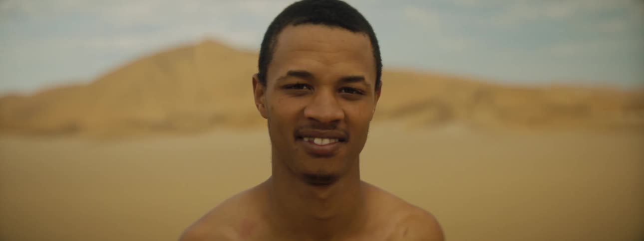 A man standing and smiling with the sky and clouds in the background