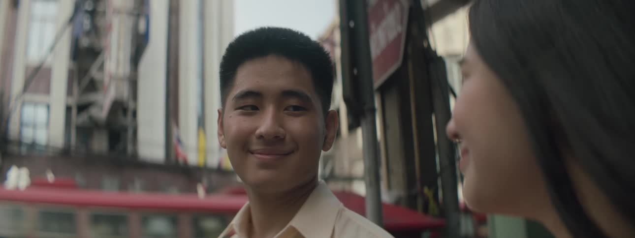 Man and woman standing near city street as bus passes turns to smile at each other