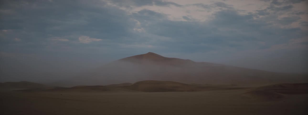 Clouds float above a sand dune in a desert at sunrise