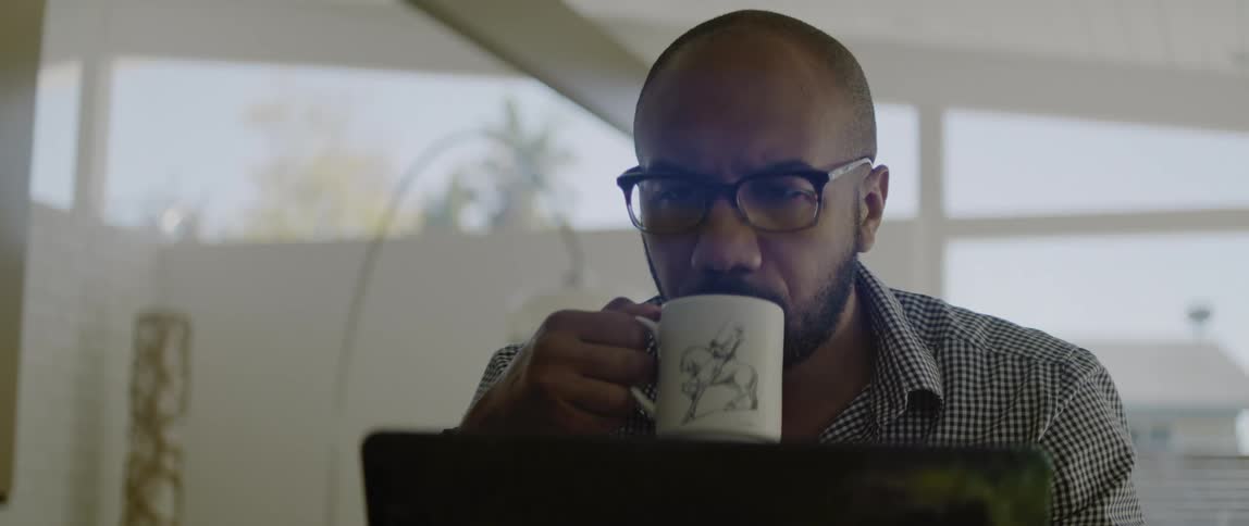 A man sipping coffee at a laptop