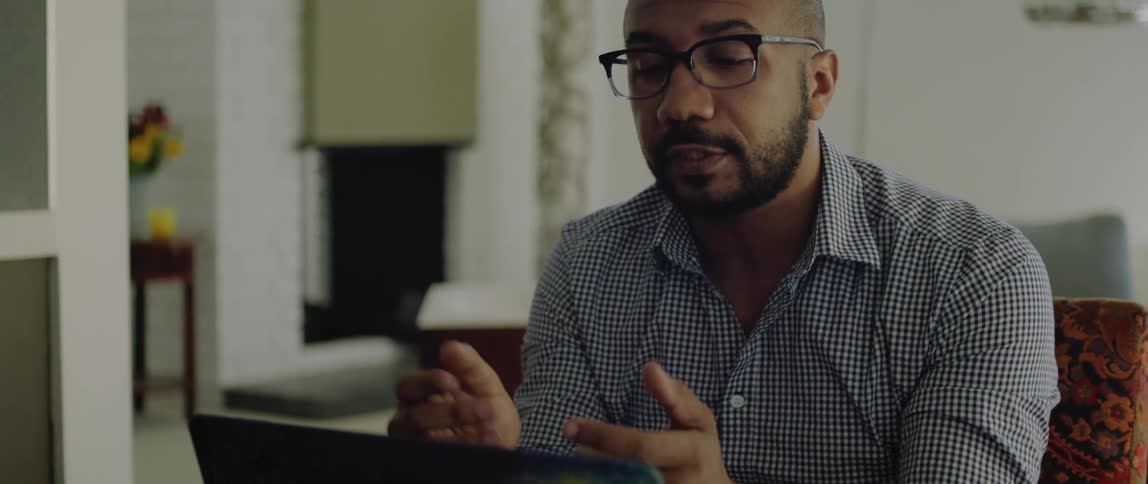 A man sits at home and talks with someone on his laptop
