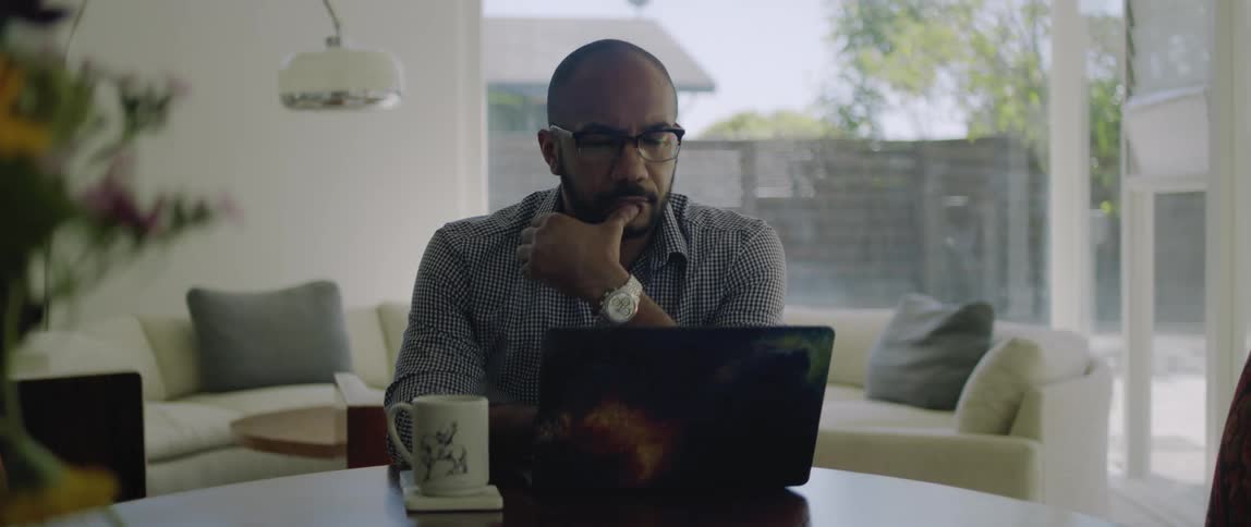 A man sits at home with a cup of coffee and looks at his laptop