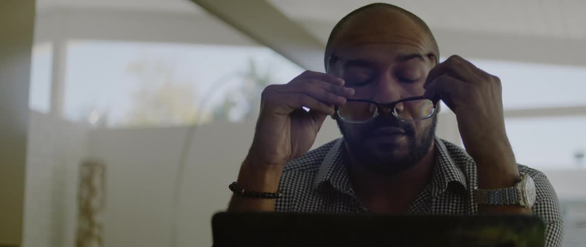 A man shakes his head while looking at laptop as he sits indoors during the day
