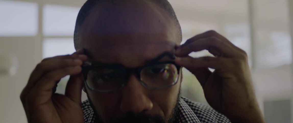 A man is indoors when he reaches for his glasses and puts them on