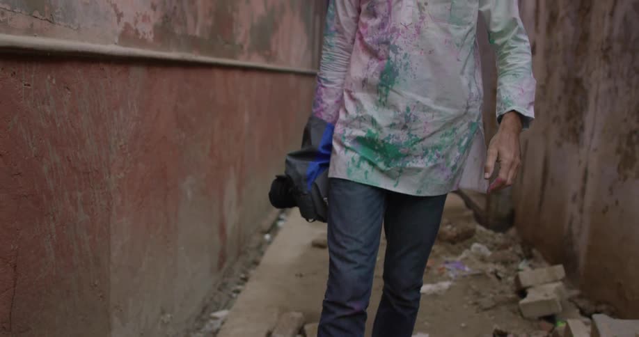 A man is walking down an alley carrying a camera