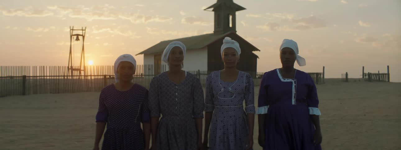 Four women walking and standing with a building the sky and clouds in the background