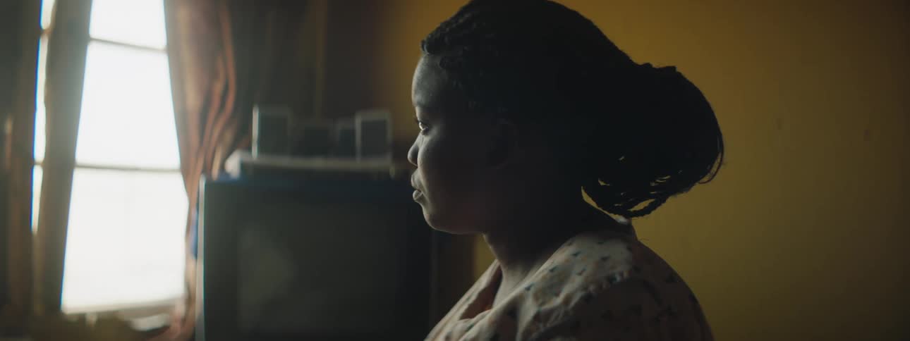 A black woman sitting at home looks out the window
