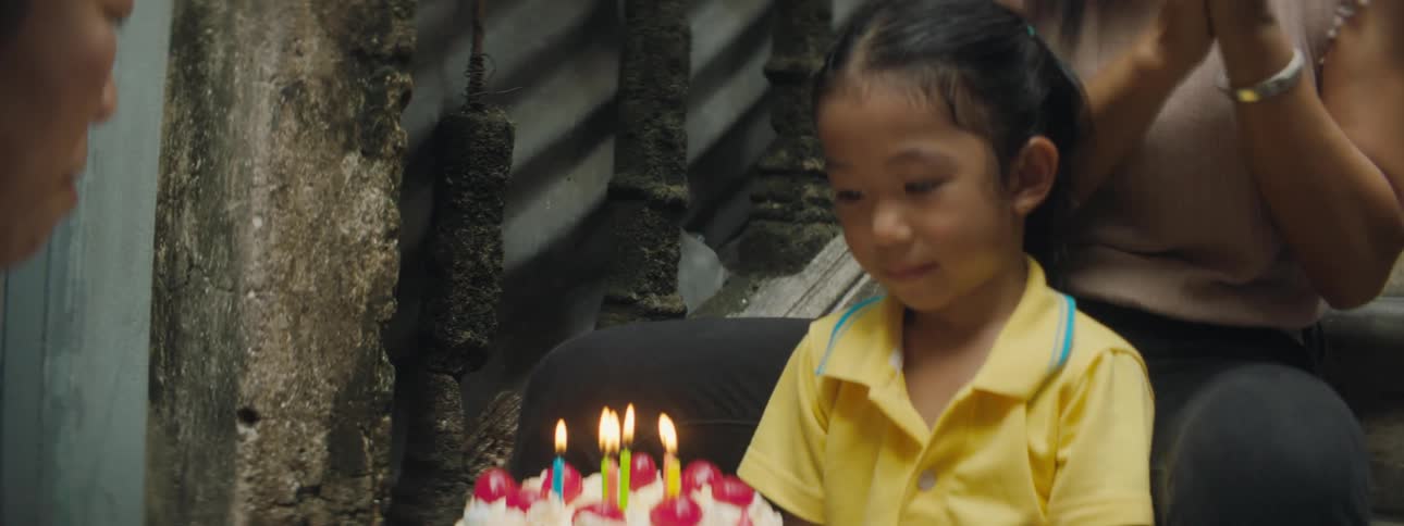 A woman brings a cake with lit candles to a young girl to out and she does