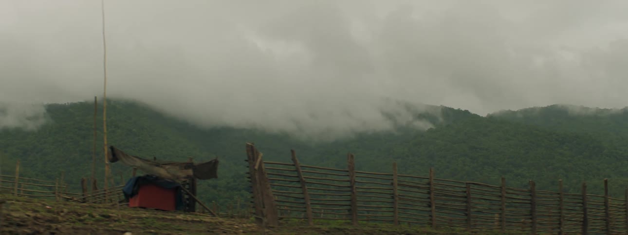 A fence with a hill fog the sky and clouds in the background