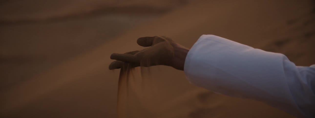 A woman on the beach with her arm outstretched allows sand to fall through her fingers