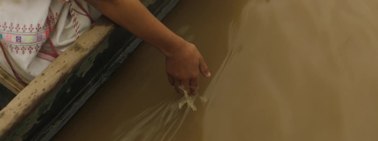 A girl dips her hand in a murky river while riding a boat