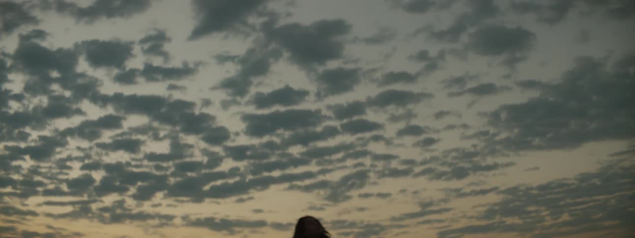 Woman sitting on sand dune is silhouetted against the sky in the desert at dusk