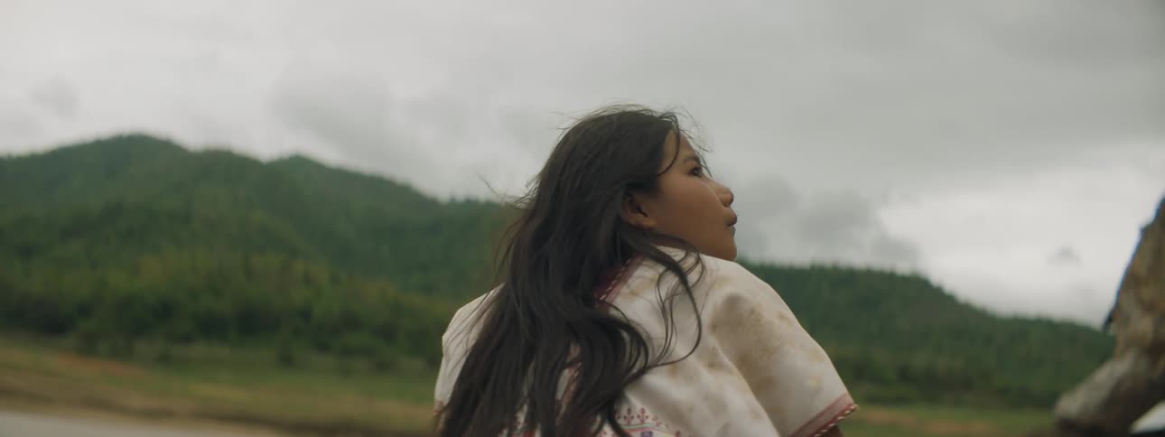 A young girl stands outside and looks up at the grey sky