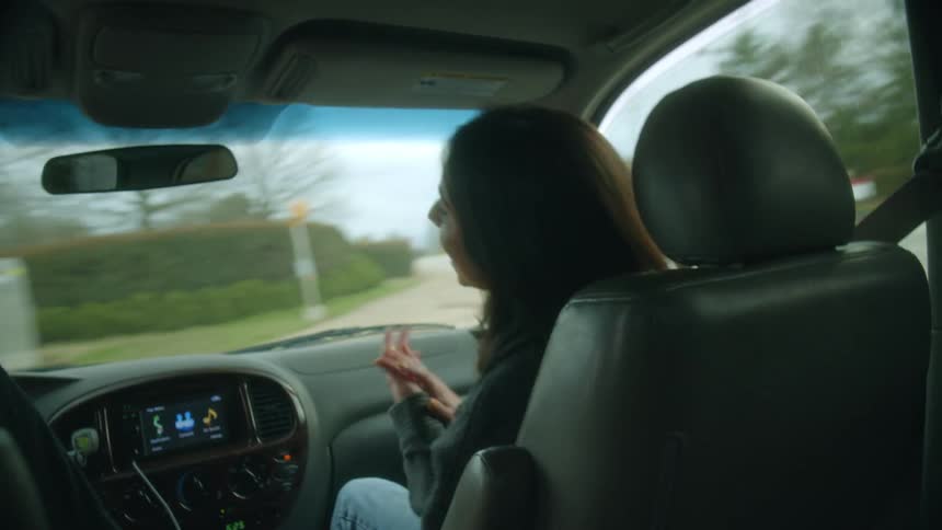 Two teenagers are laughing as they are traveling in a car and the driver turns on the streets