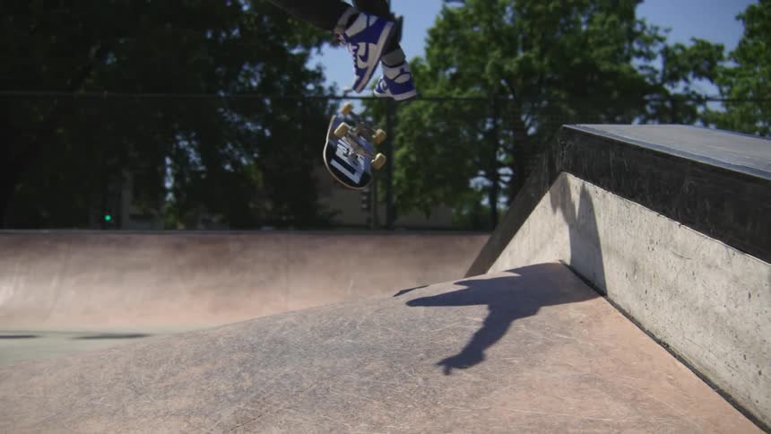 A teenage boy is riding his skateboard in a skateboard park and does a kick flip stunt