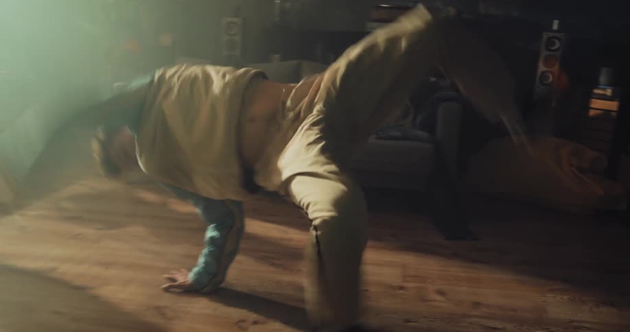 A teenage boy is sitting on the floor in front of a couch and then he does break dancing moves