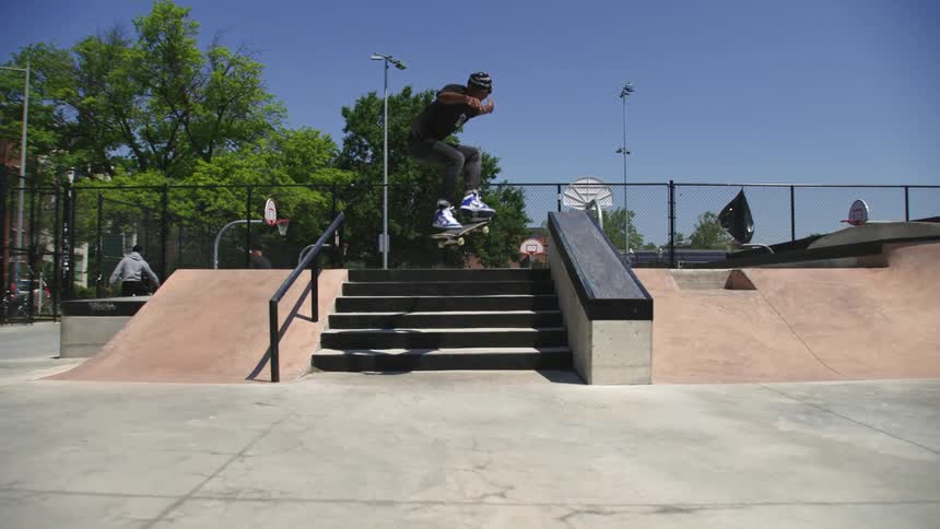 A teenager on a skateboard flies over stairs at a park and does a kick flip over them