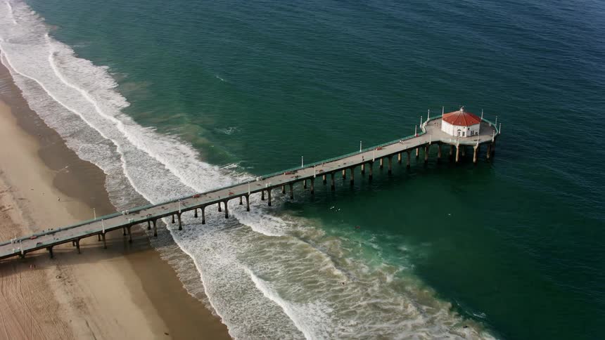 People move along pier as waves roll onto the beach near mist covering town