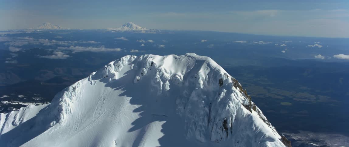A snow covered mountain peak with a view of other mountains on the horizon