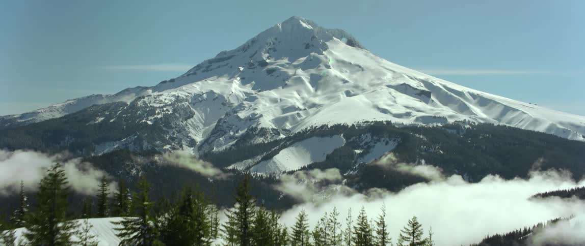 Snow covers conifer forests and mountains on both sides of valley filled with low lying clouds