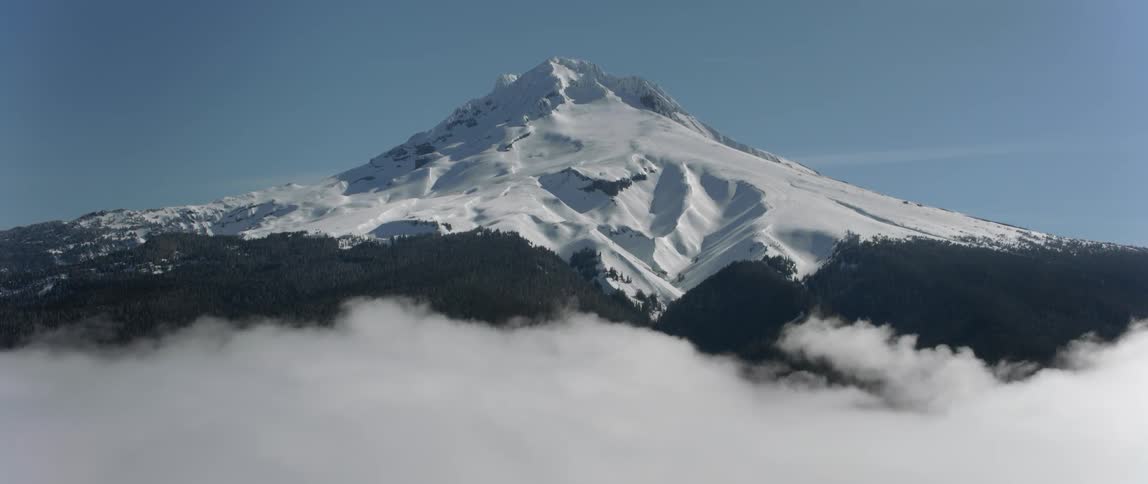 The sun shines on a snow covered mountain high above the clouds