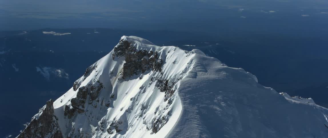 A snow covered mountain peak looming over a mountainous countryside