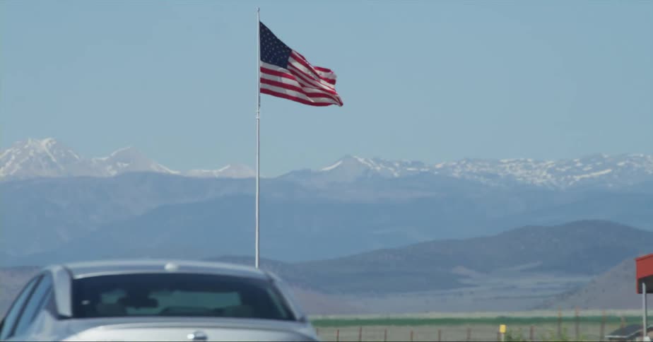 An american flag flutters atop a pole next to a road in the countryside during the day