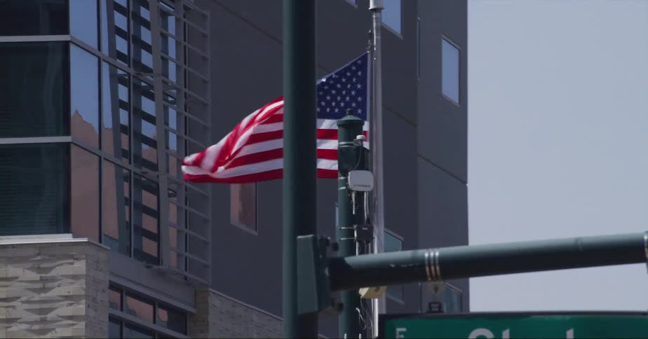 An american flag waves in the wind on a pole in front of a downtown building on the corner of clark avenue