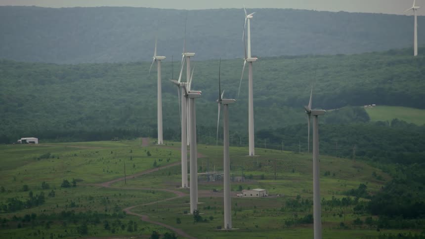 Wind turbines spin below rolling hills