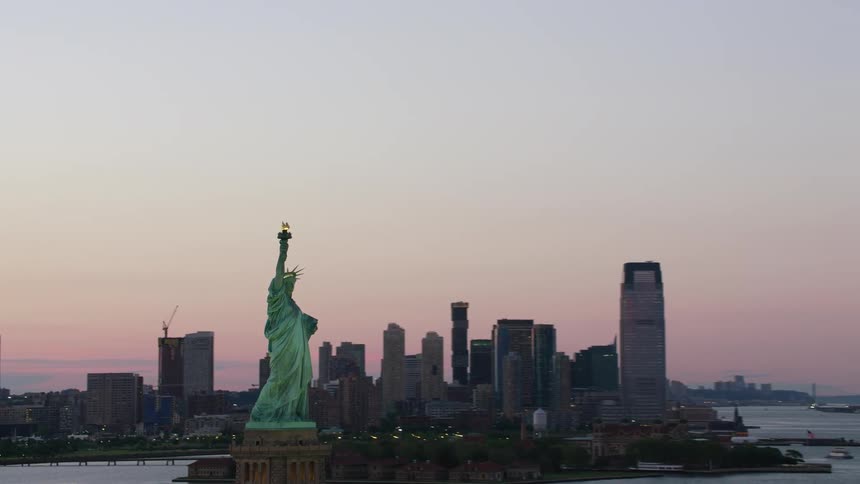 A red sky hangs over a large city with a statue on an island in the river