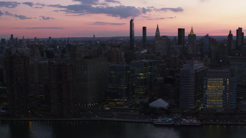 Skyscrapers in city bordering shore are silhouetted against red sky