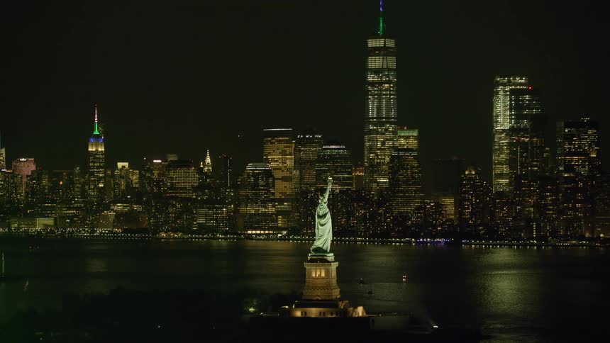 The statue of liberty overlooks new york harbor as lights illuminate city buildings