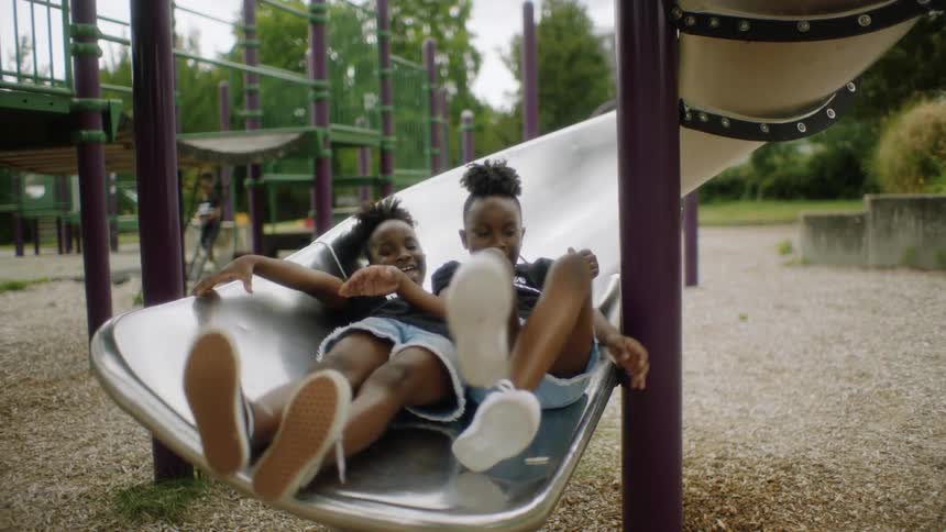 Two girls go down a slide together at a playground