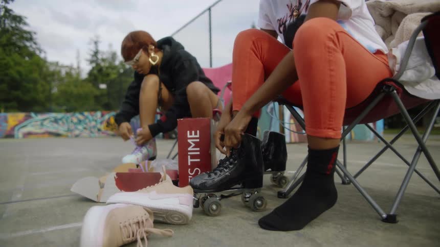 Women with orange jeans white shirt black raincoat and glasses put on roller skaters in the skatepark